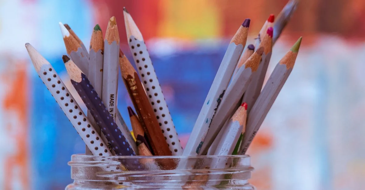 Gros plan sur des crayons en bois colorés dans un bocal en verre avec un arrière-plan flou vibrant.