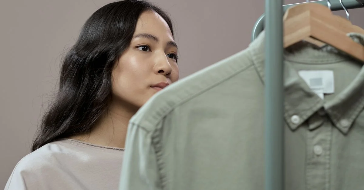 Femme asiatique parcourant des vêtements dans un studio de mode, se concentrant sur les détails.