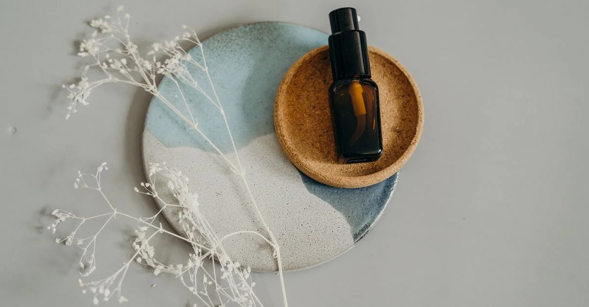 Composition élégante d'un flacon cosmétique sur des assiettes en céramique, rehaussée par de délicates fleurs séchées.