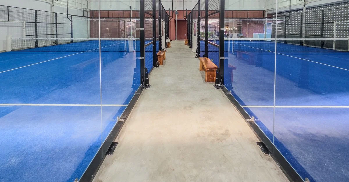 Salles de padel modernes en intérieur avec des surfaces bleues vives et des partitions en verre.