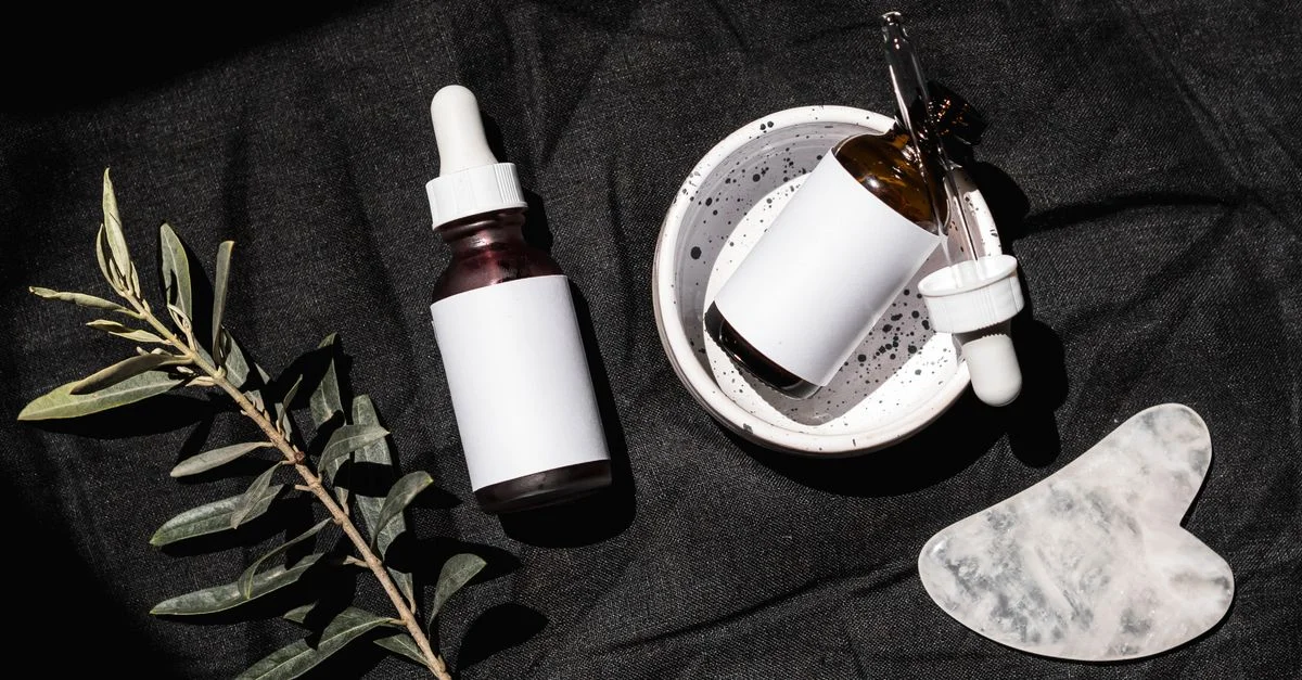 Vue de dessus de sérums pour la peau et gua sha sur un tissu noir avec des feuilles.