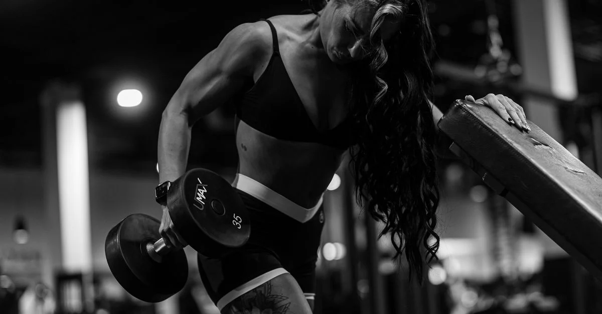 Une femme forte réalisant un entraînement avec haltères dans une salle de sport. Image en noir et blanc.