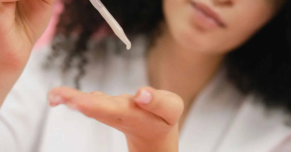 Gros plan sur une femme appliquant un sérum de soin de la peau avec une pipette, axé sur les soins corporels et l'application cosmétique.