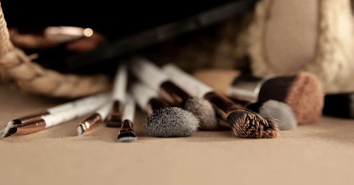 Gros plan sur divers pinceaux de maquillage sur un fond beige, mettant en valeur une disposition professionnelle de beauté.