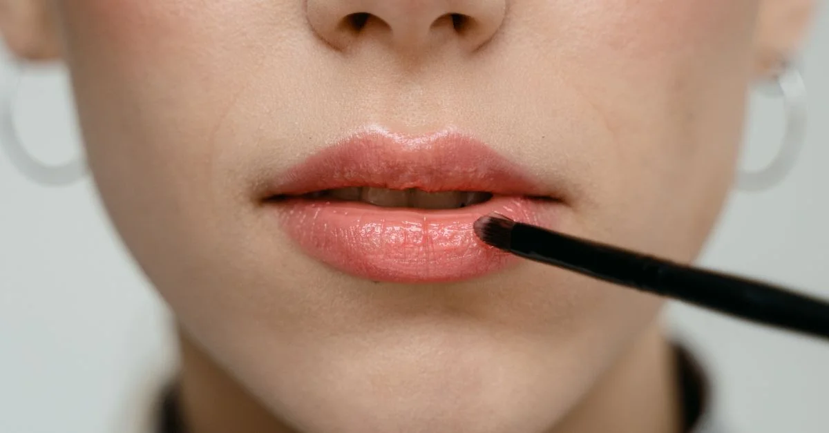 Un gros plan détaillé d'une femme appliquant du rouge à lèvres rose avec un pinceau.