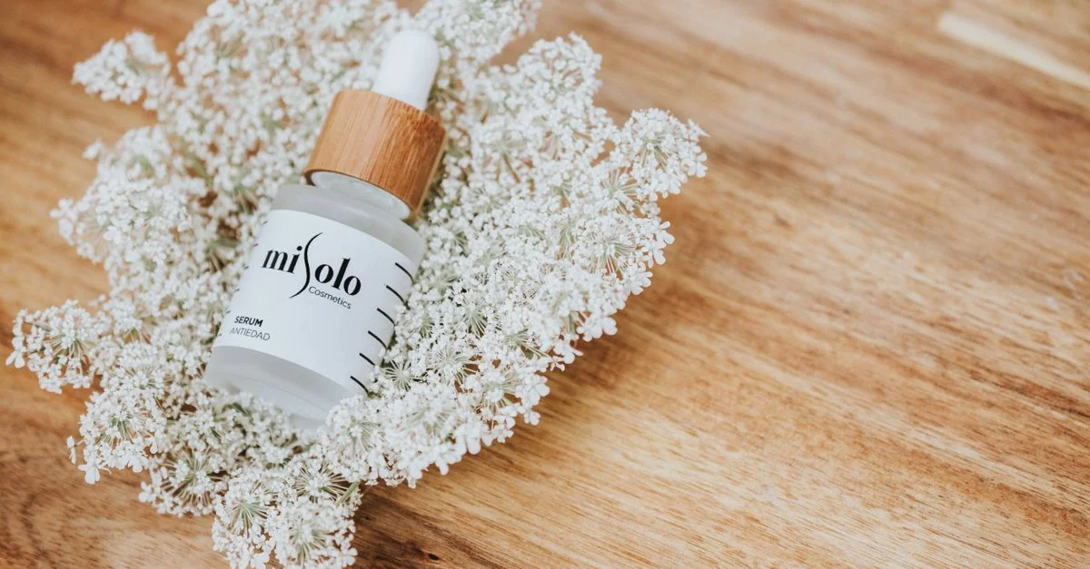 Bouteille de sérum élégante présentée avec des fleurs blanches sur fond en bois.
